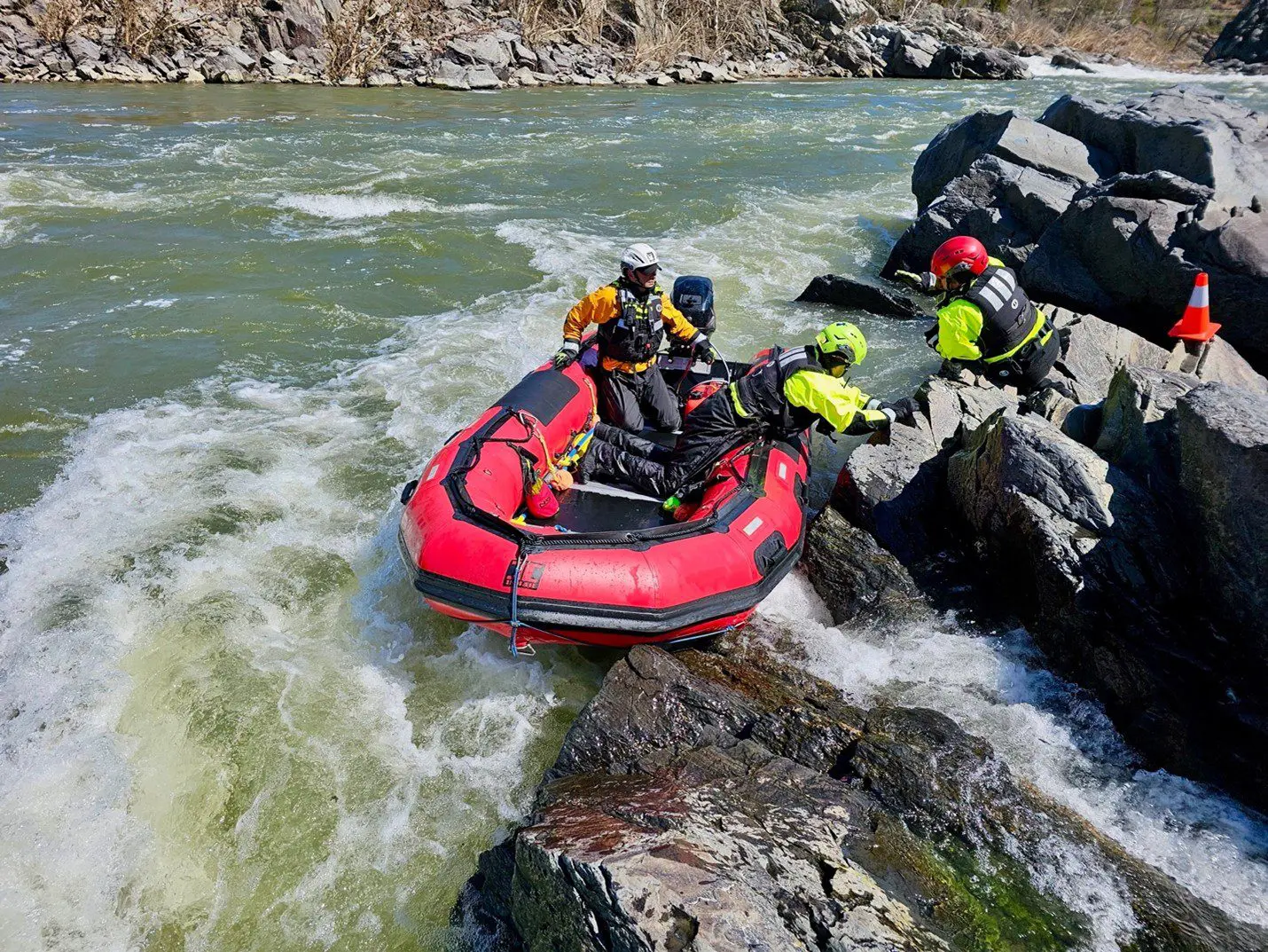 Rescue team assists inflatable raft in rocky river rapids.