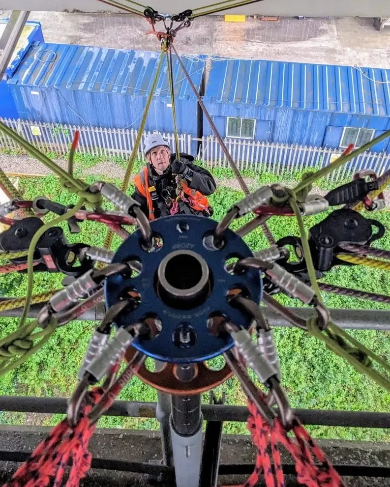 A person working on a complex mechanical device with multiple arms under a blue canopy.